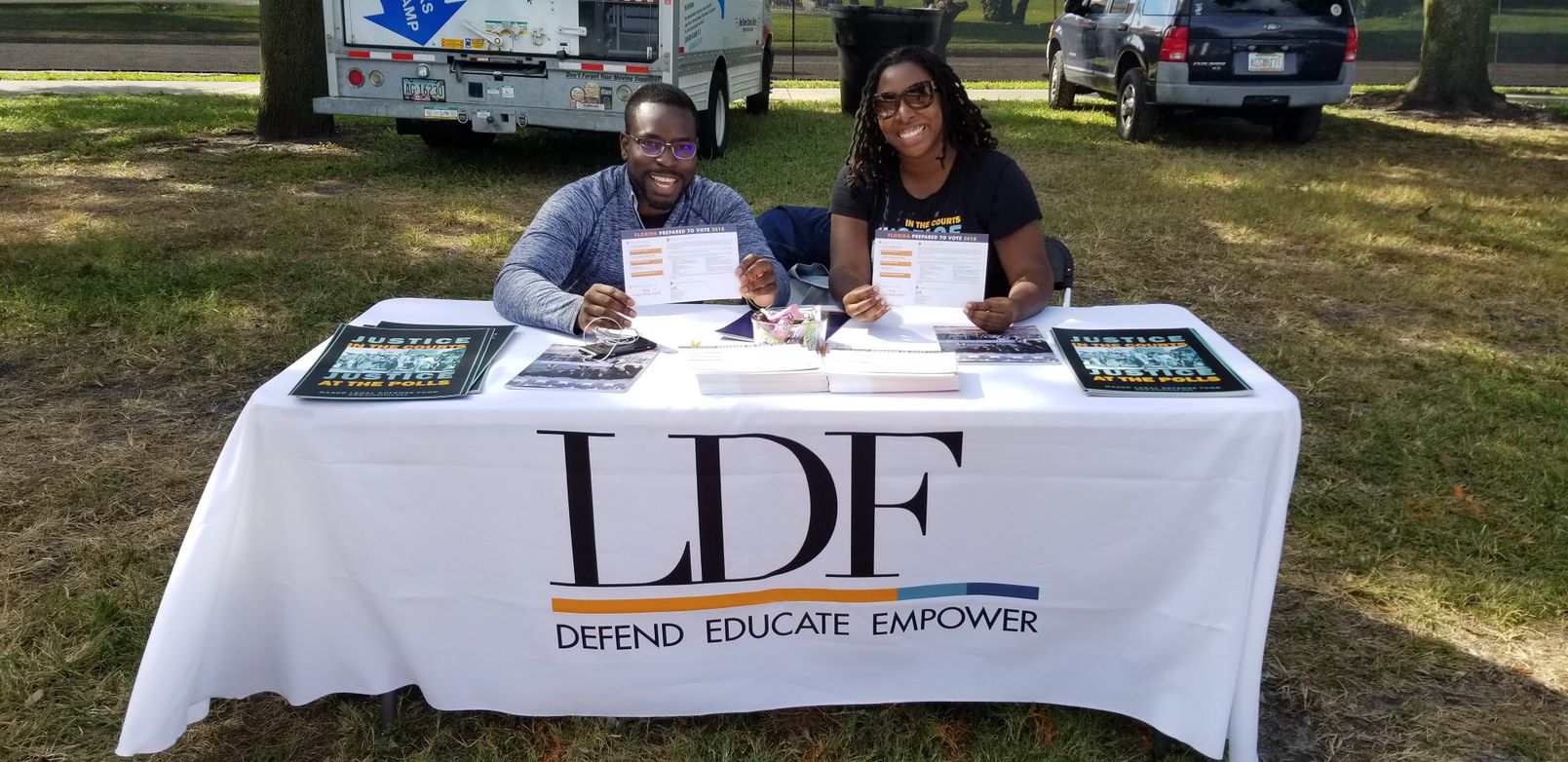 Two Black people sitting at a table holding voting signs