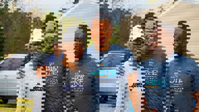 Picture of three Black people smiling with voting shirts. 