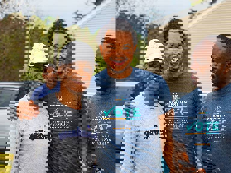 Picture of three Black people smiling with voting shirts. 